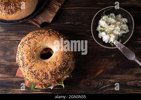 Planche à découper avec bagels au jambon et à la ricotta sur fond de bois foncé, sandwich au prosciutto et au fromage, style rustique. Banque D'Images