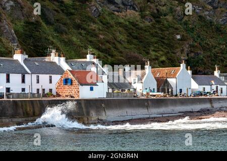 PENNAN VILLAGE ABERDEENSHIRE SCOTLAND FALAISES PULVÉRISATION DE MER SUR BRISE-LAMES ET RANGÉE DE MAISONS À LA FIN DE L'ÉTÉ Banque D'Images