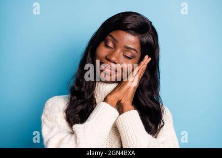 Photo de jolie peau sombre rêveuse femme habillée blanc vêtements d'hiver bras joue fermeture yeux isolé couleur bleu fond Banque D'Images