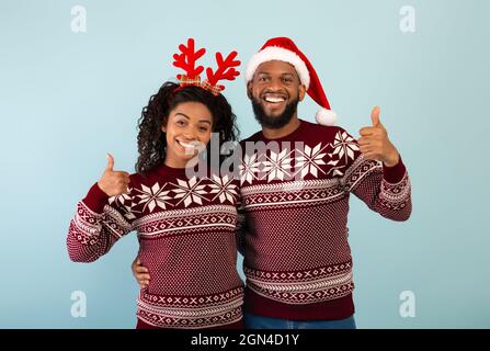 Joyeux Noël et Bonne Année. Un couple afro-américain enthousiaste avec des chandails identiques, qui se montre enthousiaste Banque D'Images