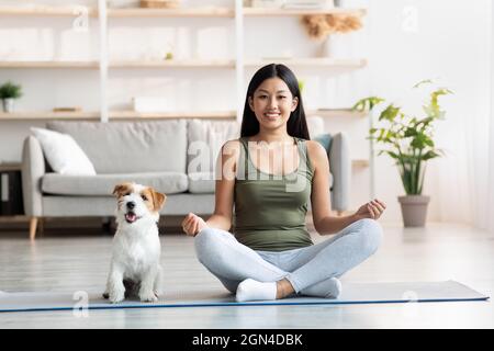 Une jeune femme positive fait du yoga avec son chien à la maison Banque D'Images