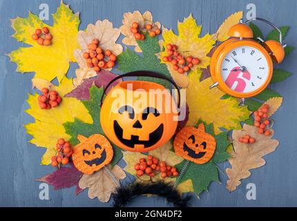 Lanterne Jack o Halloween avec bonbons sur un fond d'automne coloré de feuilles séchées, baies rowan orange et un réveil. Carte de fête d'Halloween Banque D'Images