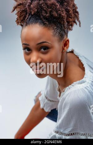 Belle jeune femme avec une expression calme regardant l'appareil photo alors qu'elle se croise sur ses hunches dans un portrait court de studio Banque D'Images