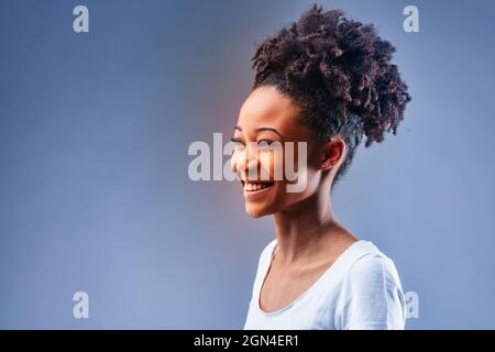 Joyeux charismatique jeune Black femme avec un sourire vif regardant à côté de l'espace sur bleu dans un portrait de studio Banque D'Images