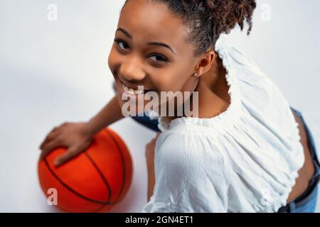 Sympathique bonne jeune femme noire souriant à l'appareil photo alors qu'elle se croche avec sa main à une balle rouge colorée dans un petit portr de studio court Banque D'Images