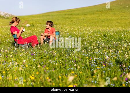 Deux touristes assis sur des chaises et profitant du petit-déjeuner dans une prairie magnifique remplie de jonquilles sauvages près du lac Kapetanovo. Banque D'Images