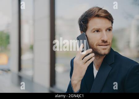 L'entrepreneur pensif masculin focalisé sur la distance fait répondre à l'appel utilise le téléphone mobile Banque D'Images