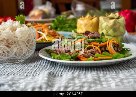 Repas vietnamien sur l'assiette, bœuf frit avec haricots verts et carottes, riz dans un bol, salade de mangue et boîte de bambou sur la table. Banque D'Images