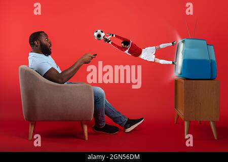 Gardien de but de football sautant hors de la télévision pendant qu'un spectateur regarde un match Banque D'Images