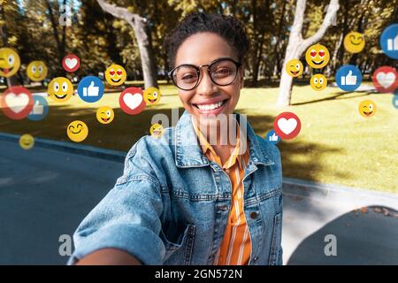 Bonne femme afro-américaine millénaire dans décontracté, lunettes fait selfie dans le parc pour les réseaux sociaux et le blog Banque D'Images