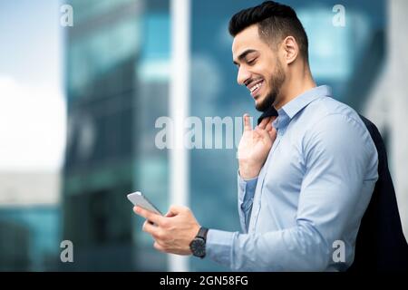 Vue latérale d'un jeune entrepreneur du Moyen-Orient qui vérifie ses e-mails sur son téléphone portable Banque D'Images