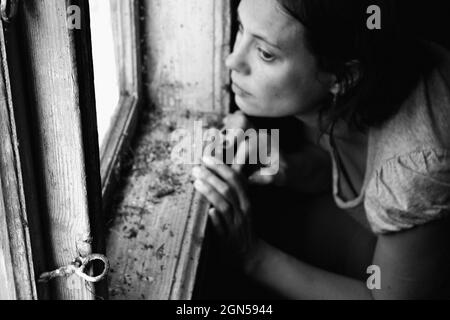 Portrait surréaliste. Femme regardant par la vieille fenêtre. Portrait d'une mystérieuse jeune femme. Photographie en noir et blanc. Banque D'Images