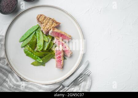 Thonière tatatatataki sésame croûte hors-d'œuvre ensemble avec des oignons de printemps et des pois mange-tout, sur plaque, sur fond de pierre blanche, vue de dessus plat, avec copyspace Banque D'Images