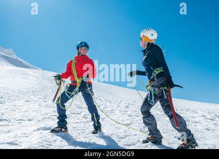 Deux rires à l'autre jeunes femmes Rope équipe montant Mont blanc du Tacul sommet 4248m vêtements d'alpinisme habillés avec des haches de glace sur la neige slop Banque D'Images