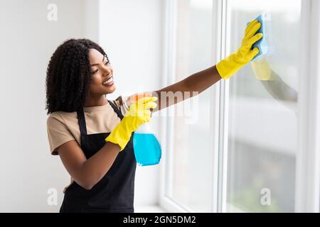 La jeune femme africaine en gants jaunes lave la fenêtre. Nettoyage de la maison Banque D'Images