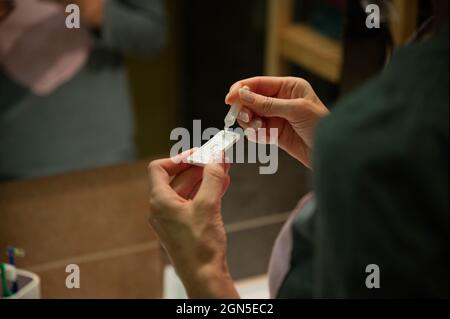 Vue sur l'épaule d'une femme faisant l'auto-test pour Covid 19, en laissant tomber la solution sur le bâton d'essai. Banque D'Images