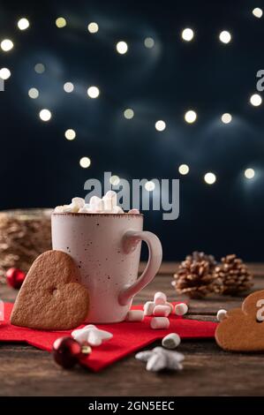 Tasse de chocolat chaud avec de minuscules marsmalows placés dans un cadre de Noël festif avec décoration et lumières en arrière-plan. Banque D'Images