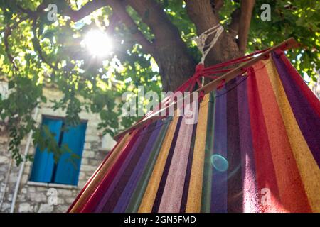 Balançant dans un hamac coloré avec le soleil brillant, branches d'arbre vertes, temps de détente d'été loisirs dans la cour traditionnelle grecque avec des murs de pierre Banque D'Images