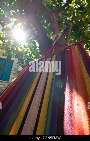 Balançant dans un hamac coloré avec le soleil briller à travers des branches d'arbre vertes, temps de loisirs d'été dans la cour traditionnelle grecque de maison avec des murs de pierre et Banque D'Images
