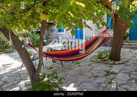 Hamac coloré et zone de loisirs avec le soleil brillant à travers les branches d'arbres verts, temps de loisirs d'été dans la cour traditionnelle grecque de maison avec pierre W Banque D'Images