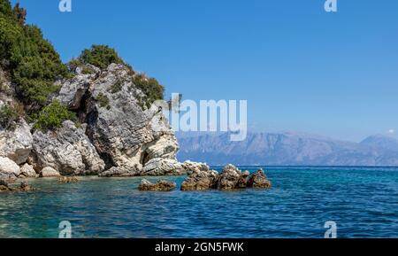 Rochers pittoresques dans les eaux bleues de la mer Ionienne avec des falaises vertes, des montagnes lointaines et un ciel lumineux. Nature d'Ormos Desimi, île Lefkada en Grèce. Été Banque D'Images