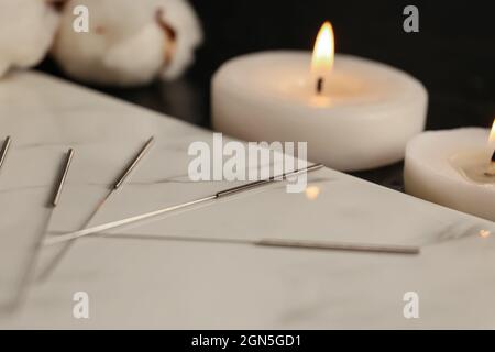 Planche avec aiguilles d'acupuncture et bougies d'arôme sur fond sombre, gros plan Banque D'Images