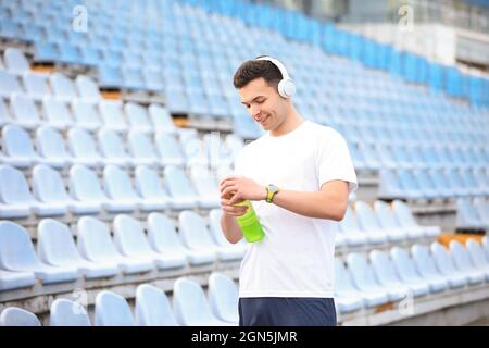 Jeune homme sportif ouvrant une bouteille d'eau au stade Banque D'Images