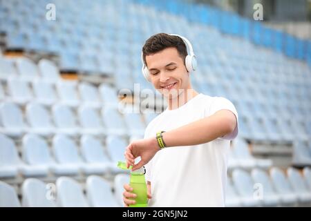 Jeune homme sportif ouvrant une bouteille d'eau au stade Banque D'Images