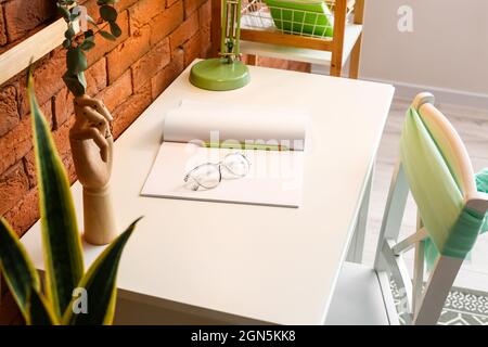 Un lieu de travail confortable avec un ordinateur portable, un crayon et des lunettes sur une table près d'un mur de briques Banque D'Images