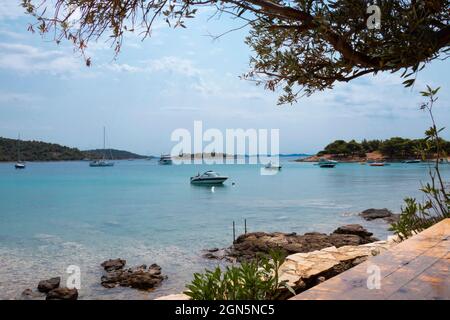 Kosirina, Murter, Croatie - 24 août 2021 : bateaux amarrés dans une baie calme, vue du bar de la plage à travers la végétation Banque D'Images