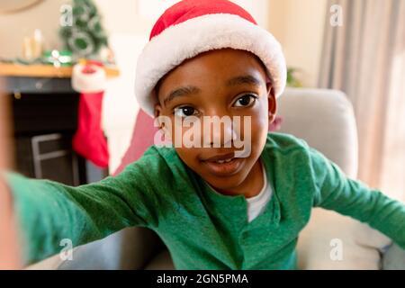 Un garçon afro-américain portant un chapeau de père noël et prenant un selfie à l'heure de noël Banque D'Images