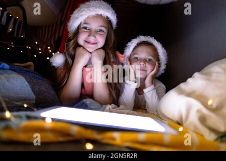 Joyeux frères et sœurs caucasiens portant des chapeaux de père noël et utilisant une tablette à l'heure de noël Banque D'Images