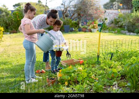 Bonne mère, fille et fils caucasiens arroser les plantes ensemble Banque D'Images