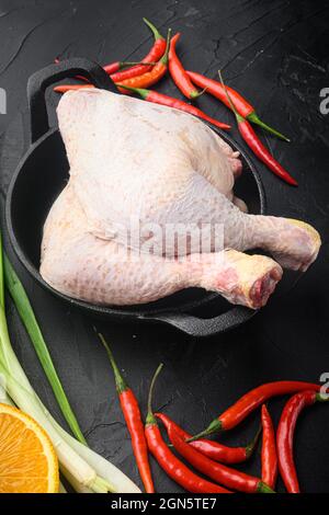 Pilons de poulet frais, jambes avec ingrédients pour la cuisson, avec orange et piment, sur poêle à frire en fonte, sur fond de pierre noire Banque D'Images
