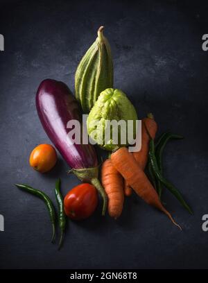 divers légumes biologiques sur une surface texturée foncée, vue du dessus de l'aubergine, des carottes, des tomates, de la gourde striée, de la chayote et des piments verts Banque D'Images