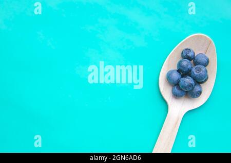 Plat de cuillère recyclée et de bleuets frais juteux sur la table de couleurs. Espace pour le texte. Fruits mûrs et mûrs de la myrtille dans une cuillère écologique sur fond turquoise. CopySpace. Aliments végétariens crus sains Banque D'Images