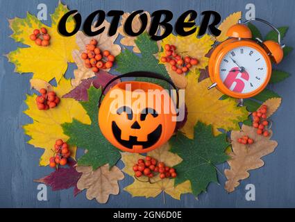 Forme de citrouille avec un sourire de Jack o lanterne effrayant, réveil orange et l'inscription OCTOBRE sur un fond de feuilles séchées, baies de rowan sur un gr Banque D'Images