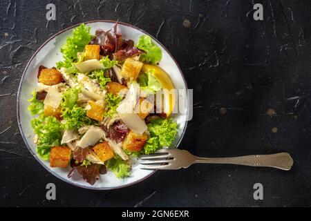 Salade César au poulet, prise d'en haut sur fond noir avec un endroit pour le texte. Feuilles de laitue, croûtons croustillants et filet de poulet Banque D'Images