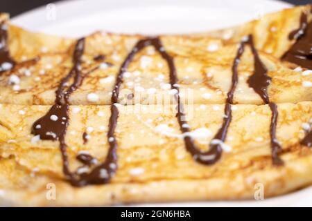 Vue rapprochée d'une crêpe au chocolat servie sur une plaque en céramique blanche. Concept gastronomique Banque D'Images