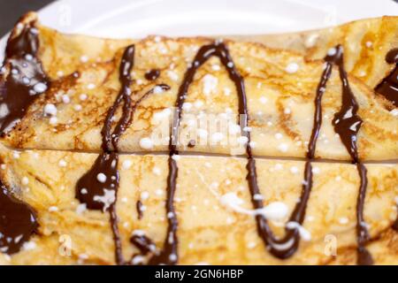 Vue aérienne rapprochée d'une crêpe au chocolat servie sur un plat blanc. Concept gastronomique Banque D'Images