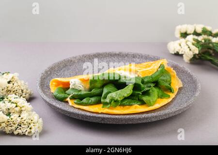 Omelette farcie aux épinards et au fromage pour le petit déjeuner, avec fleurs sur la table Banque D'Images