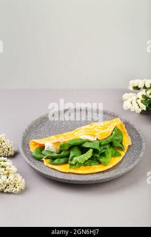 Omelette farcie aux épinards et au fromage pour le petit déjeuner, avec fleurs sur la table Banque D'Images