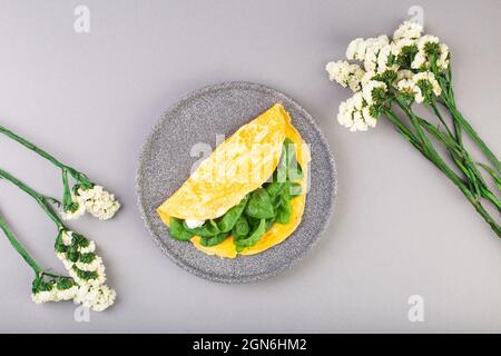 Omelette farcie aux épinards et au fromage pour le petit déjeuner, avec fleurs sur la table Banque D'Images