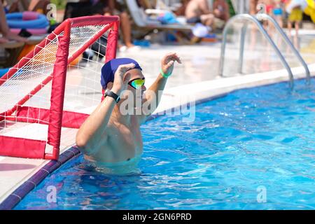 Un jeune homme se tient à la porte de la piscine et joue au water-polo à proximité Banque D'Images