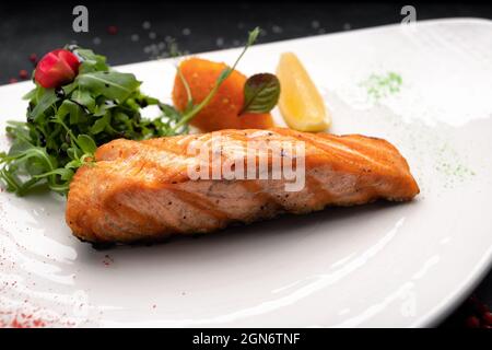 Steak de saumon frit aux herbes et au citron sur une assiette blanche sur fond sombre Banque D'Images