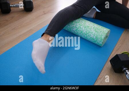 Femme de fitness dans les vêtements de sport allongé sur le tapis de yoga s'exerçant avec le rouleau en mousse Banque D'Images