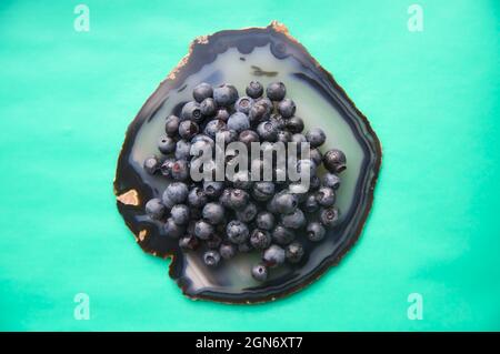 Plat de pierre précieuse agée et de bleuets frais juteux sur table turquoise. Fruits de myrtille doux isolés sur une surface en cristal translucide sur fond blanc. Copier l'espace. Aliments végétariens crus sains Banque D'Images