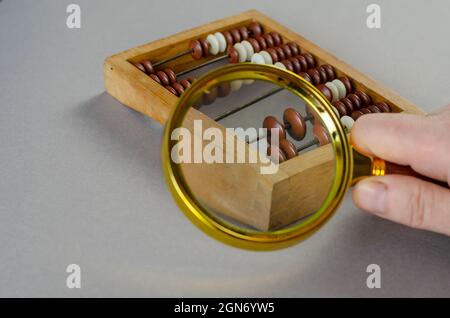 L'homme tient la loupe sur le petit abacus en bois. Grande loupe Banque D'Images