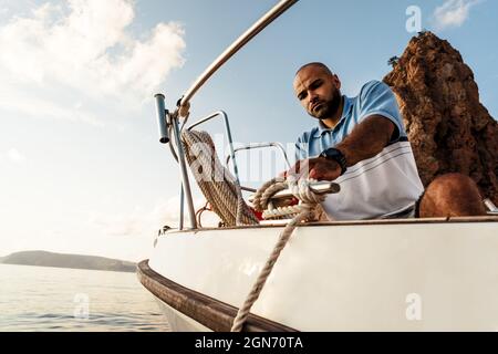 Un jeune marin afro-américain noue des cordes sur un voilier dans la mer au coucher du soleil Banque D'Images