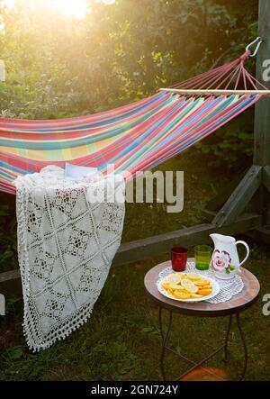 Coin détente dans le jardin. Cadre extérieur en été. Hamac. Tranches d'orange, de verres et de carafe sur une petite table basse. Banque D'Images